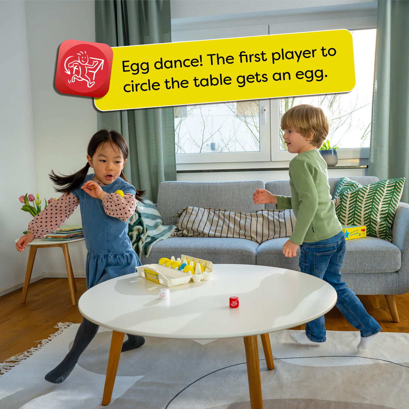 Two children playing a game around a table with HABA Dancing Eggs on it, in a living room setting. Text overlay says "Egg dance! The first player to circle the table gets an egg."