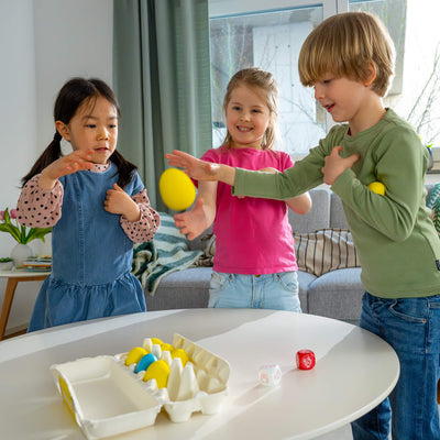 Three children playing with HABA Dancing Eggs game on a table in a living room.