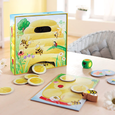 Hanna Honeybee game setup with beehive box, wooden Hanna Honeybee, green wooden die, round honey pieces, and round flower pieces