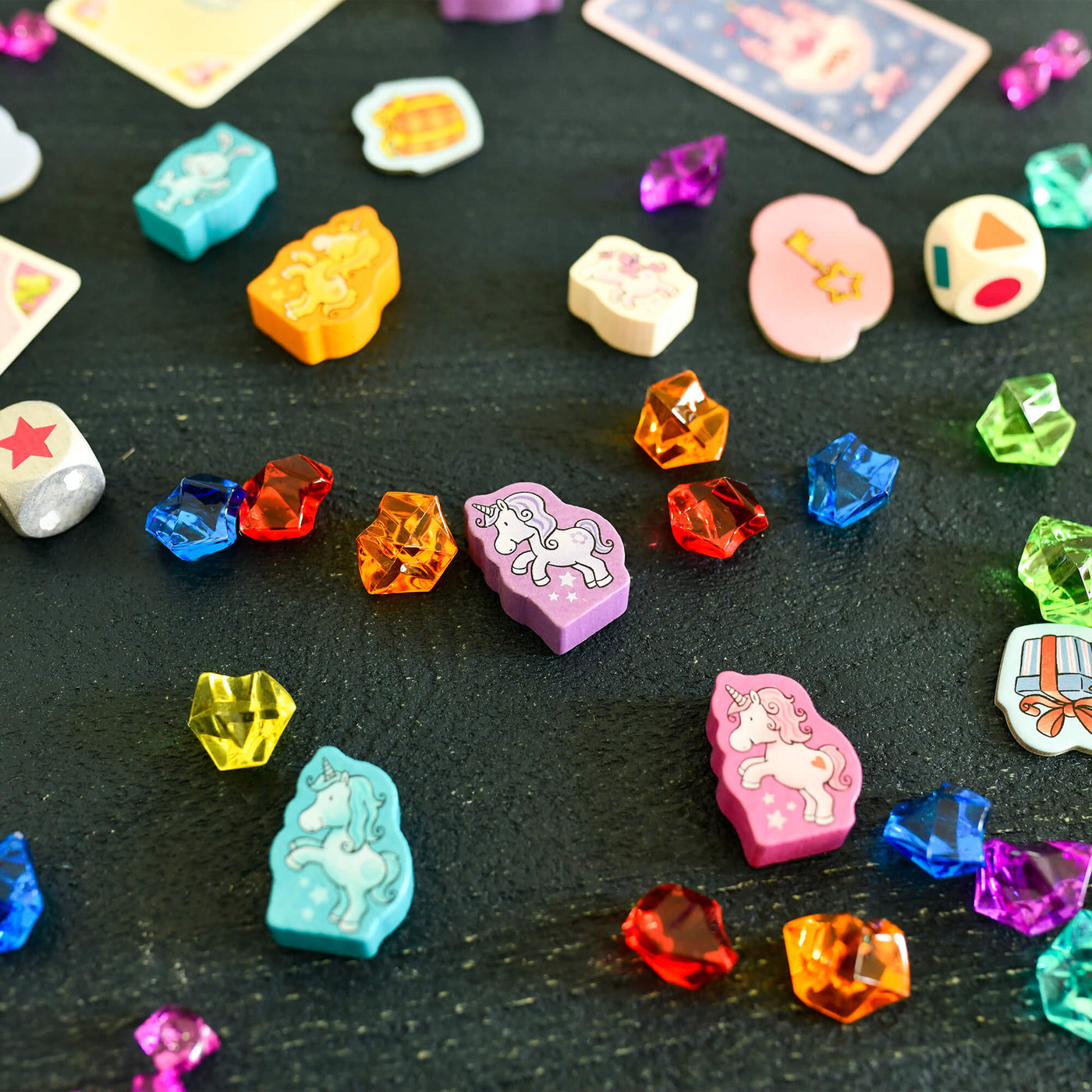 Colorful gemstone-like game pieces on a dark surface from the game Unicorn Glitterluck - Game Collection