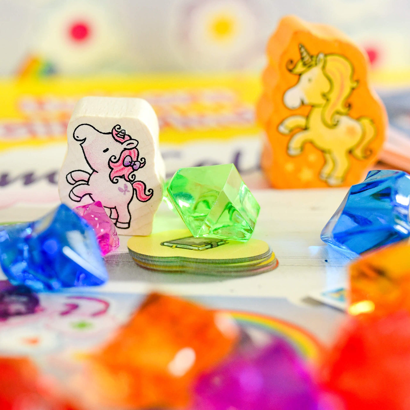 Colorful unicorn-themed game pieces on a blurred Unicorn Glitterluck - Game Collection game box