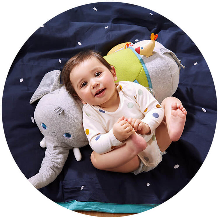 A cheerful baby laying on an Elephant Discovery Pillow on a navy blanket.