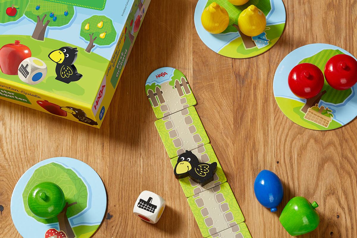 HABA First Orchard board game setup with fruit pieces, a raven game piece, and illustrated box.