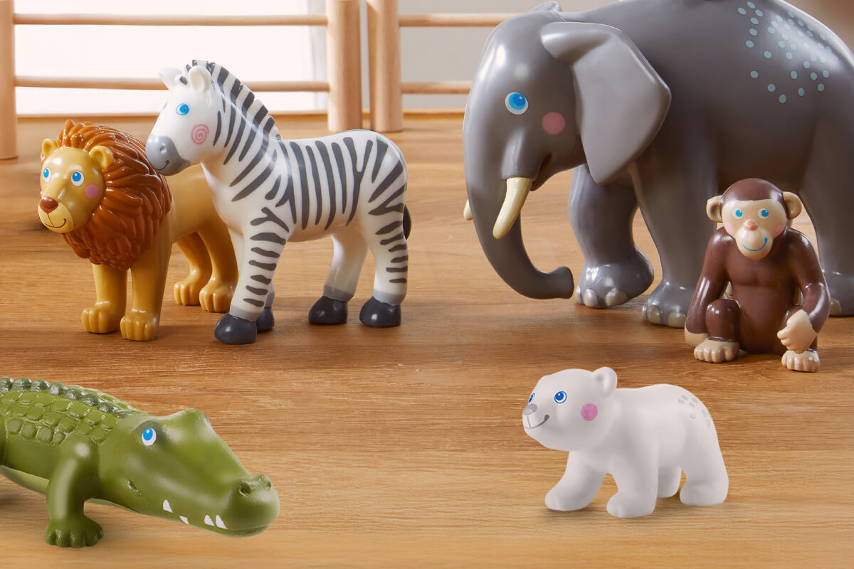 A group of HABA Little Friends toy animals including a lion, zebra, elephant, monkey, crocodile, and polar bear on a wooden surface.