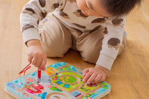 Child playing with HABA Town Maze colorful magnetic maze board on a wooden floor.