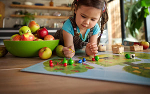 Child playing with Orchard board game on a kitchen counter with apples and a green bowl.