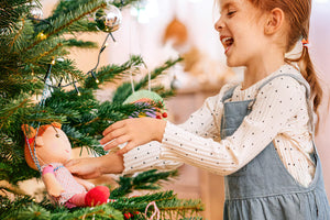 Girl smiling while decorating a Christmas tree with a HABA Roya plush doll.
