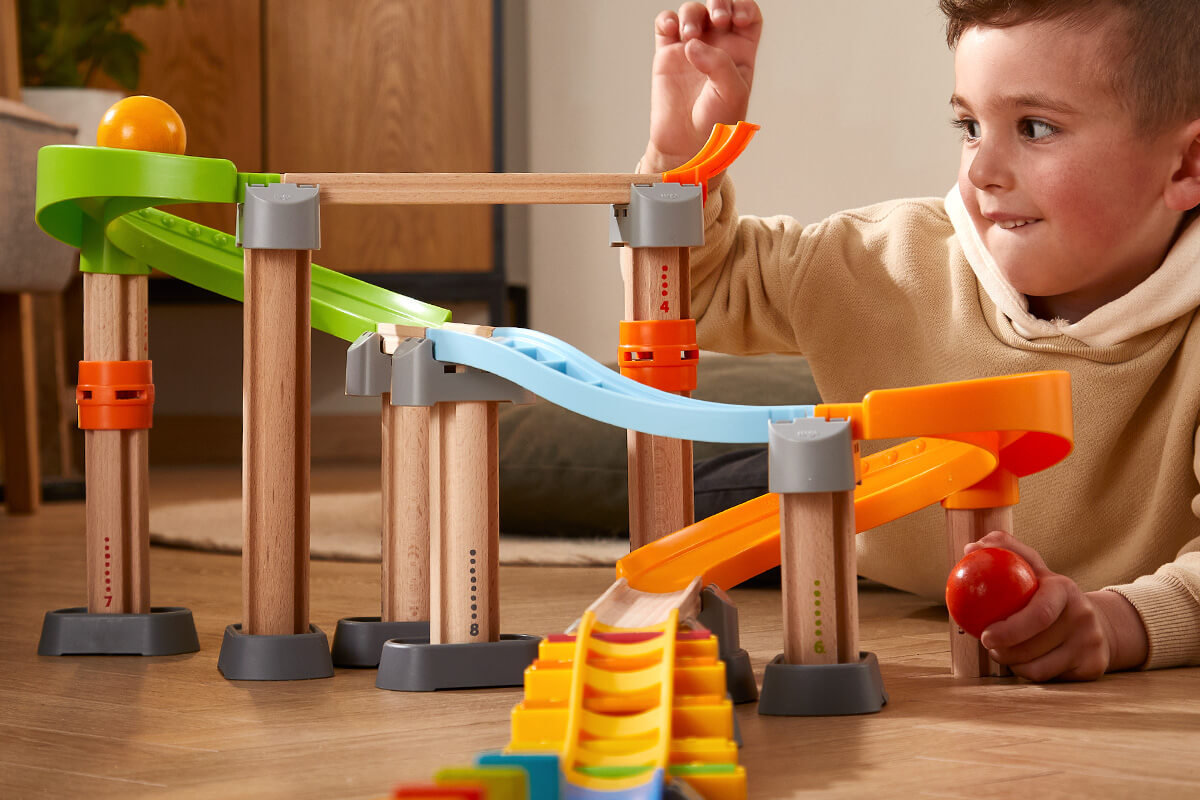 Child playing with a Kullerbu marble run toy featuring colorful tracks and wooden support beams.