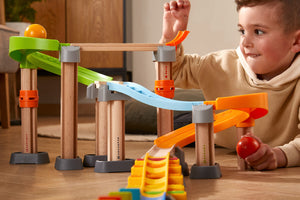 Child playing with a Kullerbu marble run toy featuring colorful tracks and wooden support beams.
