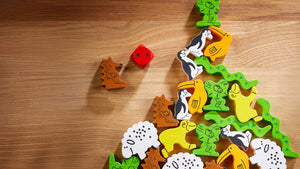 Colorful wooden animal pieces from Animal Upon Animal Game and a red die on a wooden surface.