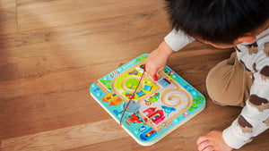 A child plays with a Town Maze colorful wooden maze toy on a wooden floor.