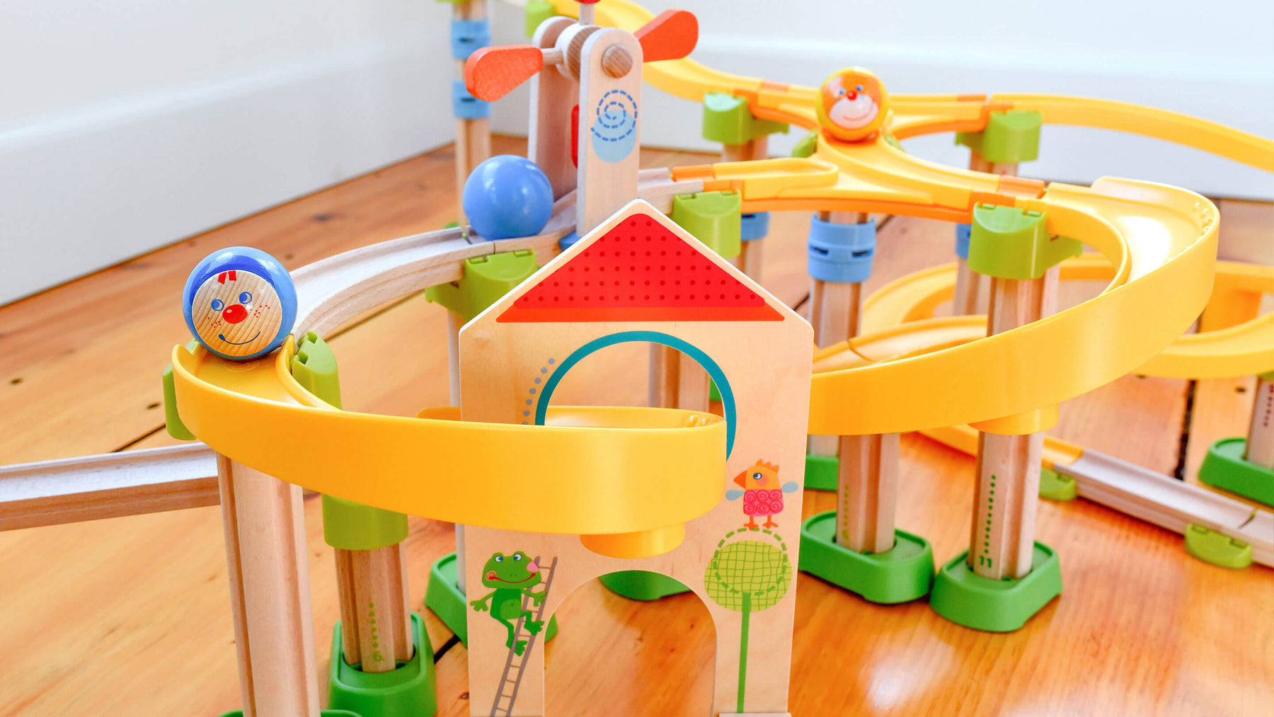Colorful wooden marble run toy on a wooden floor with yellow tracks and playful ball designs.