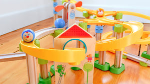 Colorful wooden marble run toy on a wooden floor with yellow tracks and playful ball designs.