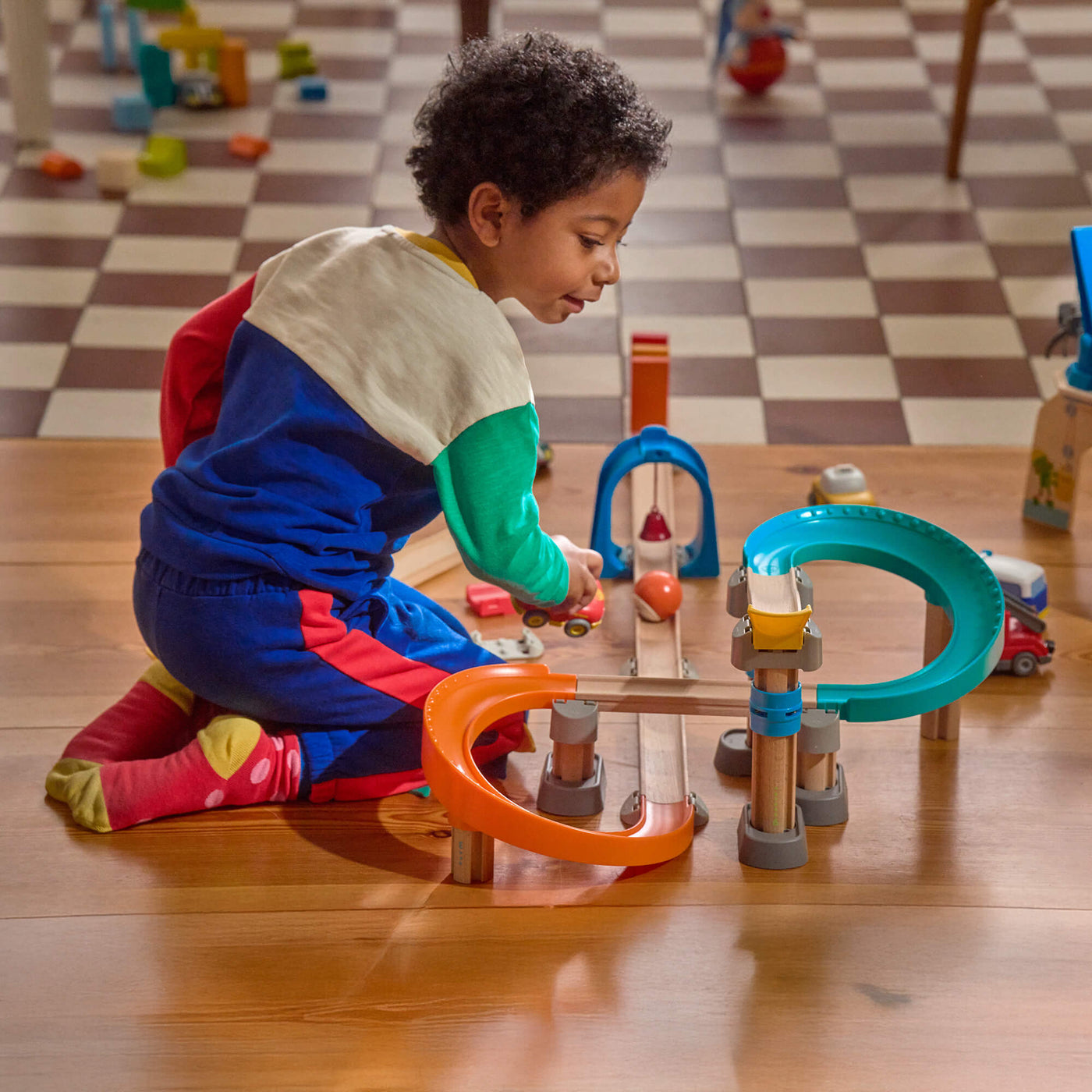 Child playing with Kullerbu Colorful Curves - Build & Grow Ball Track Set on a checkered floor