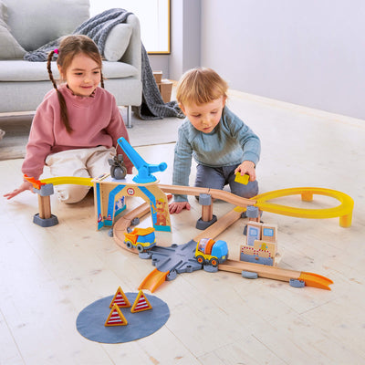 Two children playing with a Kullerbu Construction Zone Play Track Set on a light wood floor.