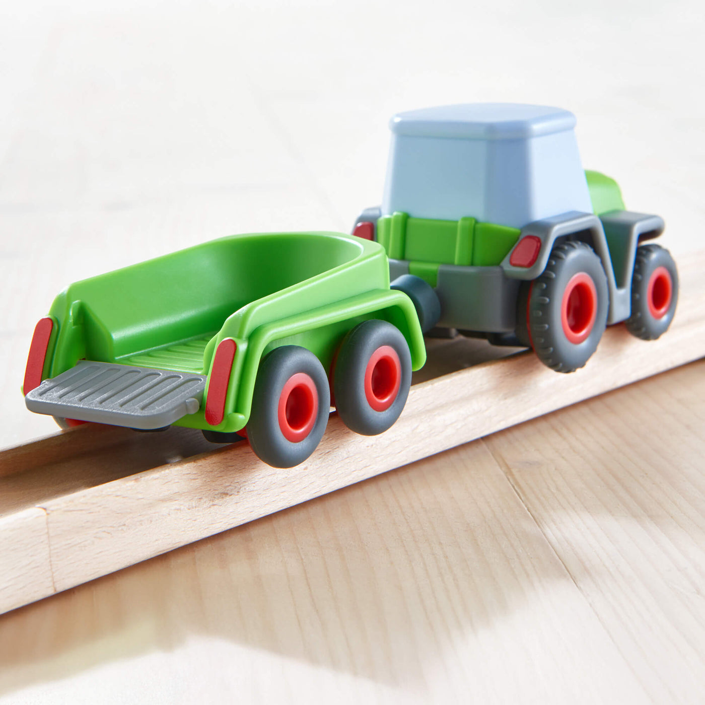 Toy tractor with a green trailer on wooden tracks