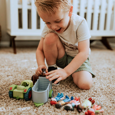 Boy putting a toy horse into the trailer of the Little Friends Tractor and Trailer set while small dolls are lined up on the carpet next to him