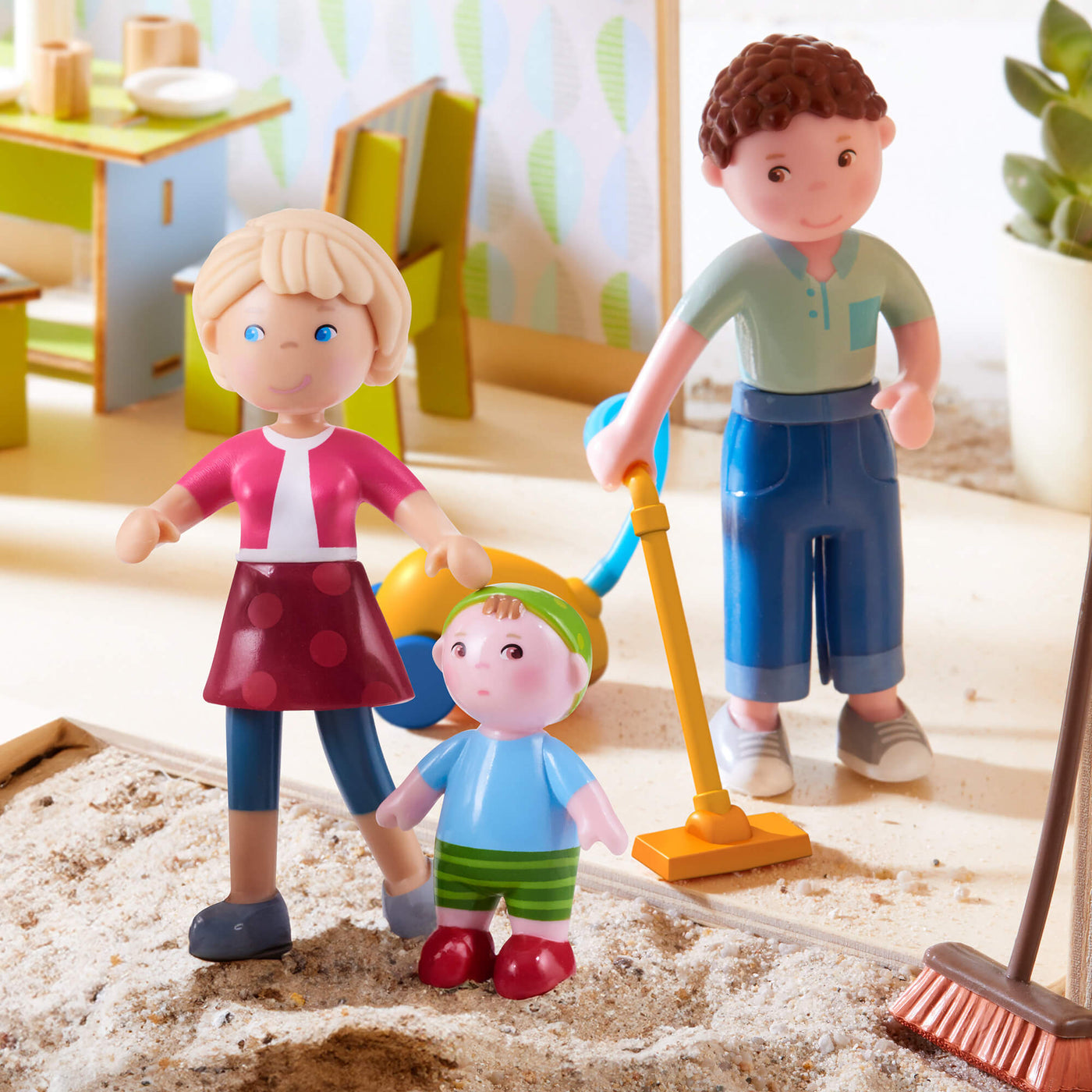 Little Friends Michael, Melanie and Baby Kilian figures cleaning up sand with a broom and toy vacuum.