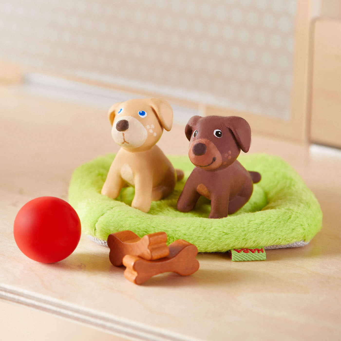 HABA Little Friends Puppy Love Playset with 2 puppies sitting on green bed, red ball, and 2 bones