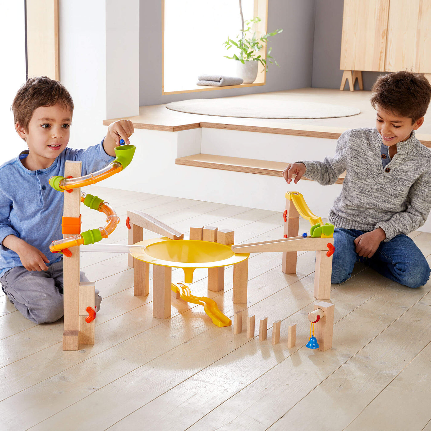 Two young boys planning with Marble Run Funnel Jungle Starter Set on wooden floor in living room