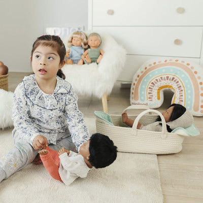 A child playing with a Miniland doll next to the cotton basket doll carrier.