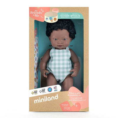 Miniland Realistic Montessori Black boy doll with curly hair, wearing a blue gingham romper, standing in the box he comes packaged in.