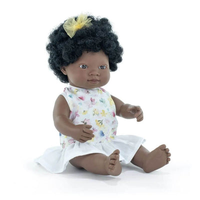 Miniland Montessori Black girl doll with curly hair and yellow bow, wearing a floral top and white skirt, seated on a white background.