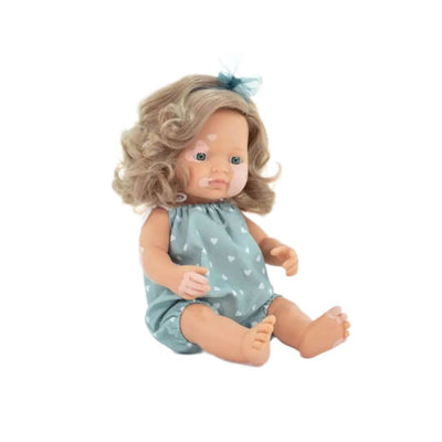 Miniland Realistic Montessori Doll of a white girl with blonde curly hair and vitiligo, wearing a teal polka-dot romper and matching bow, seated against a white background.