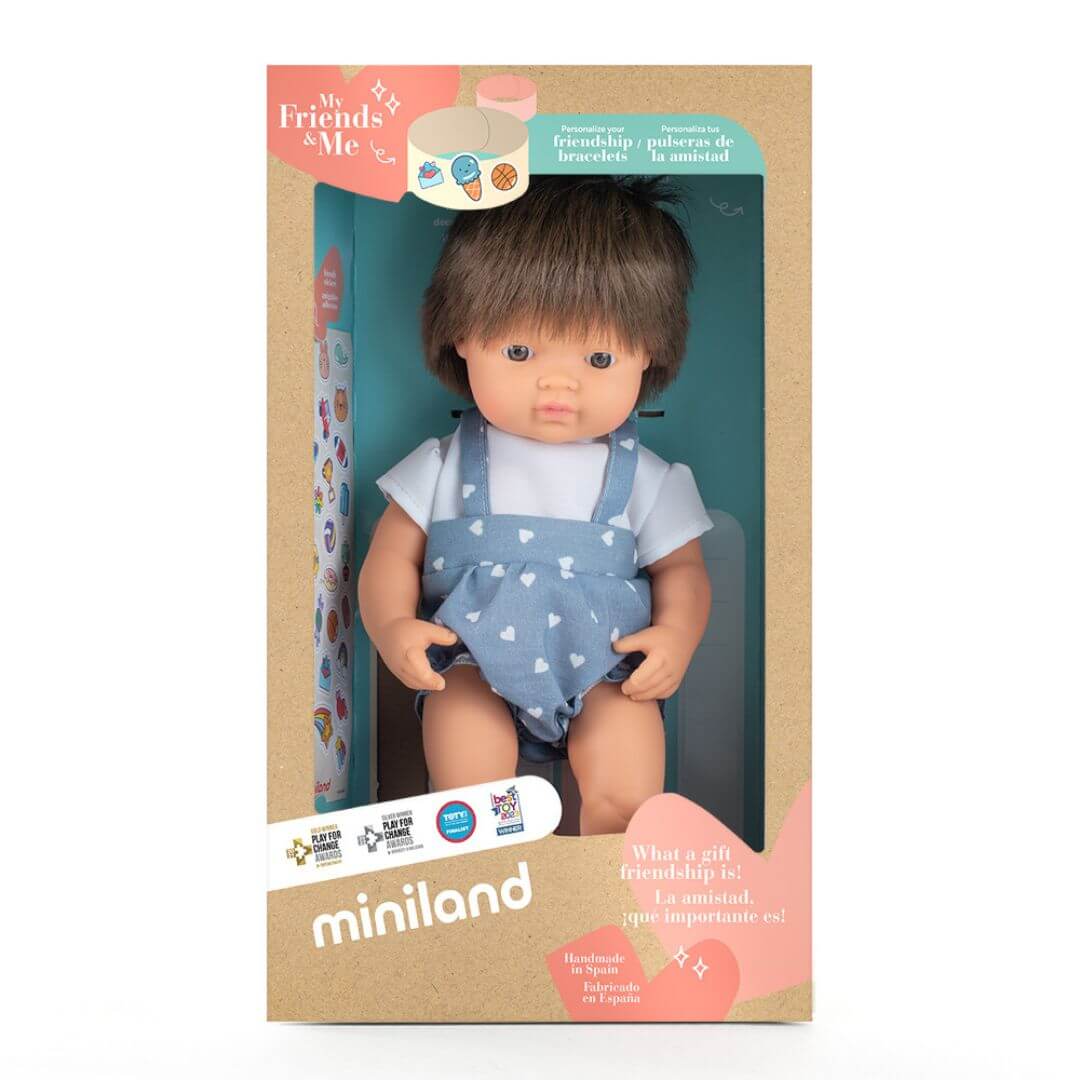 A realistic white boy doll with brown hair, dressed in a light blue romper with white heart patterns, standing up in the box he is packaged in. 