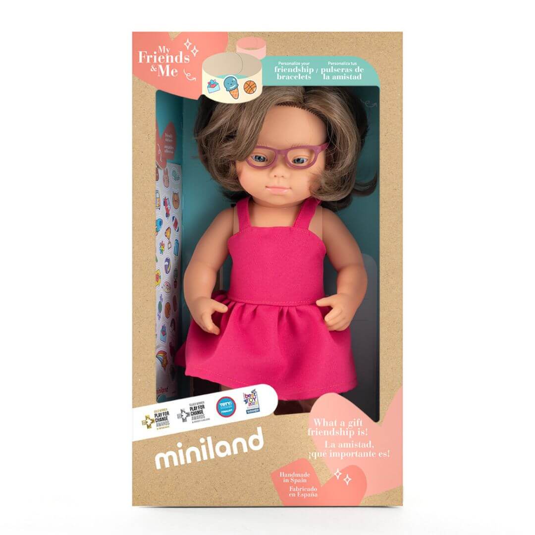 iniland realistic Montessori girl doll with Down syndrome, wearing glasses and a bright pink dress with a tulle bow headband, in the box that she arrives in.