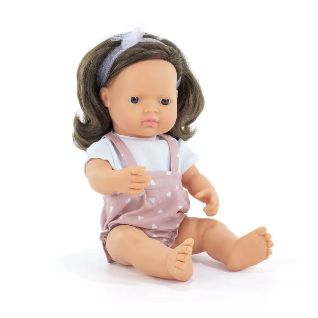 Miniland Montessori girl doll with soft brown hair, wearing a pink polka dot romper and headband, sitting upright on a white background.