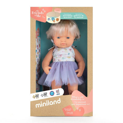 Miniland Montessori doll with blonde hair and visible cochlear implant, wearing a floral top and lavender tulle skirt, standing in the box that she is packaged in.