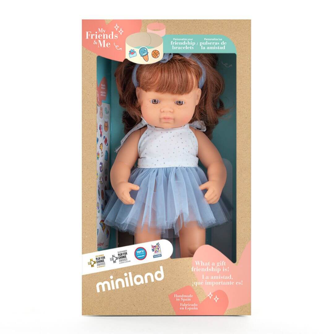 Miniland Montessori red-haired girl doll wearing a blue tulle skirt and white top with matching bow, standing in the box she is packaged in.