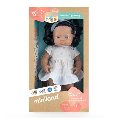 Miniland Montessori Hispanic girl doll with dark curly hair, wearing a white dress with a bow, standing in the pakagin that she arrives in.