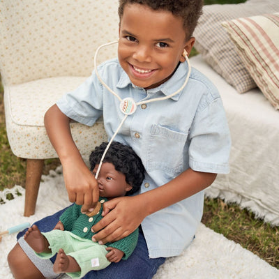 Young child playing doctor with a Miniland doll, using a toy stethoscope from the Miniland Doll-Sized Doctor Kit.