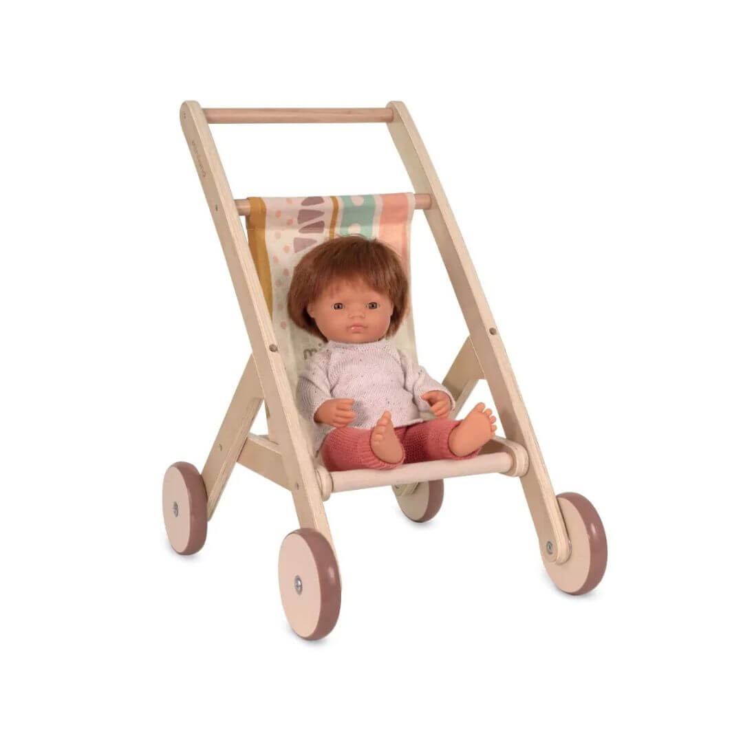 Wooden doll stroller by Miniland, made in Spain from sustainable wood with a colorful fabric seat—with a Miniland doll with short brown hair and wearing a sweater and orange knit pants.