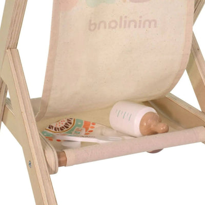Wooden doll stroller by Miniland, made in Spain from sustainable wood with a colorful fabric seat—showing the back of the stroller filled with a wooden doll bottle and other baby doll accessories.