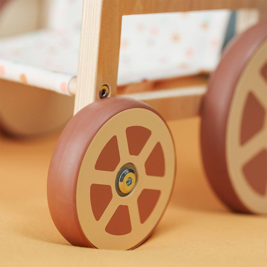 A close up of the wheels of the Miniland Wooden Doll Wheelchair showing the polka dot fabric seat and natural wood frame, designed to fit 14-inch dolls.