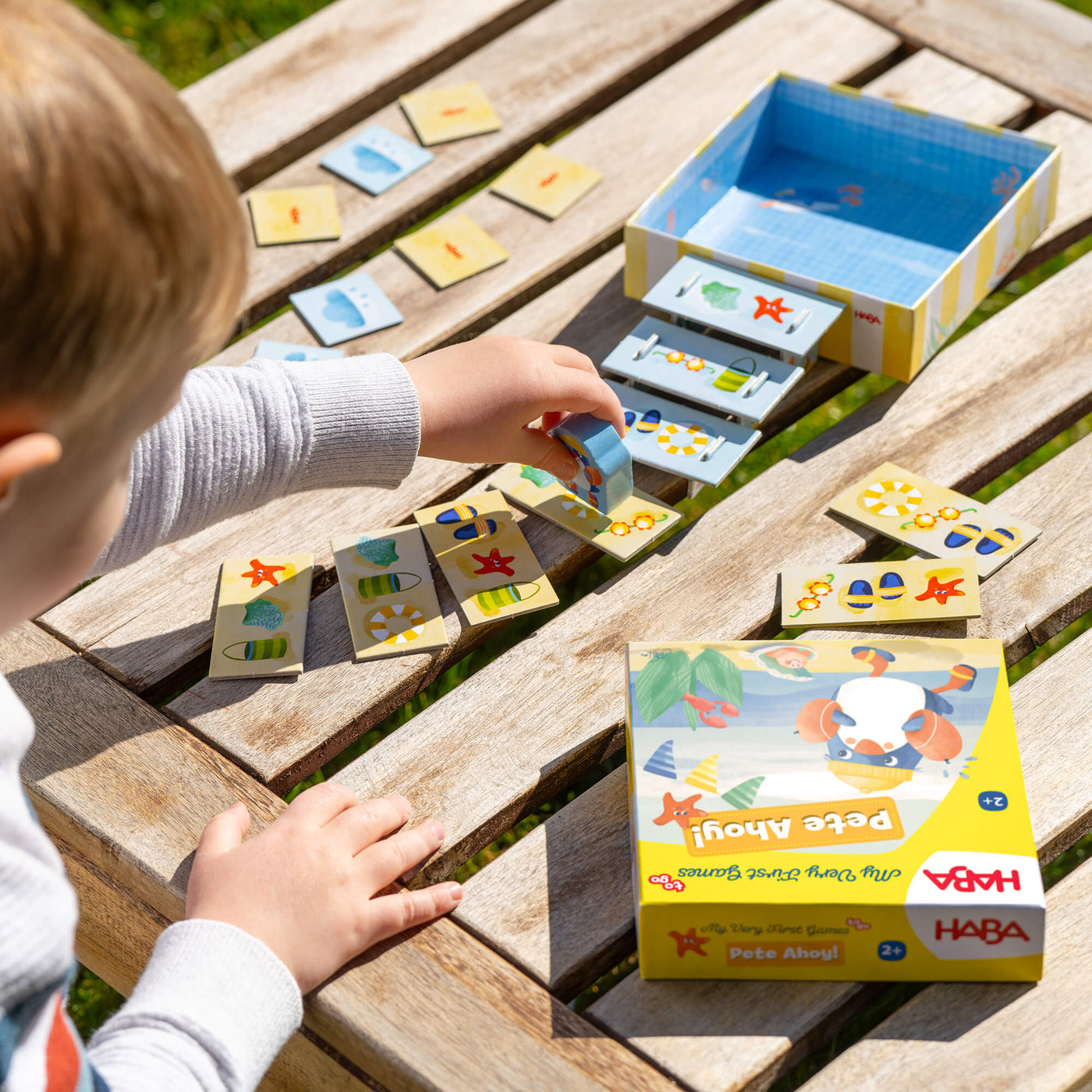 Child playing with My Very First Games To Go - Pete Ahoy! on a wooden table outdoors