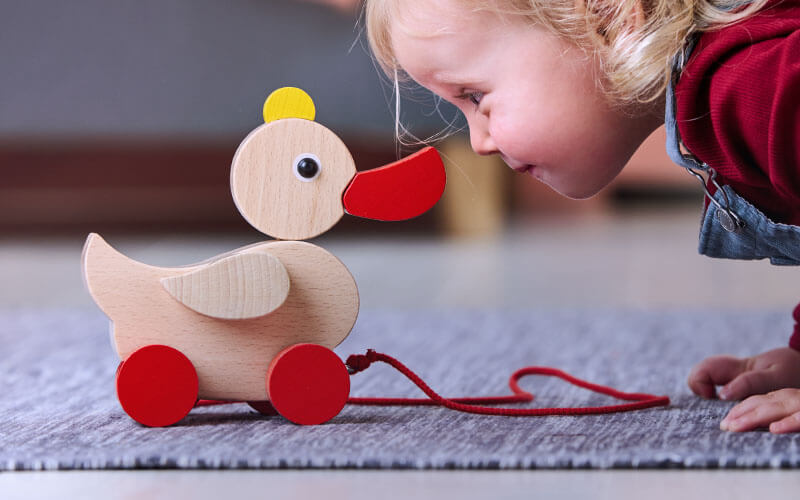 Child on floor looking face to face with HABA's Original Waddling Duck Pull Toy