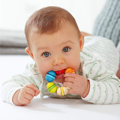 Baby on their tummy playing with a HABA Rainbow Rattle Grasping and Teething Toy