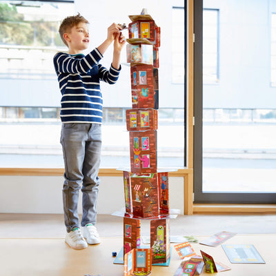 Boy standing and placing a monkey game piece on the edge of a card tower