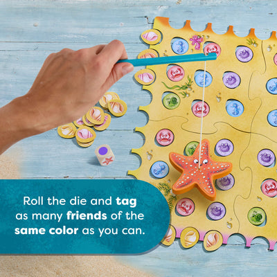 HABA Sebastian Seastar colorful game board with tiles and dice on a wooden surface, text reads 'Roll the die and tag as many friends of the same color as you can.'