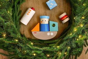 HABA Discovery Boat Wooden Building Blocks Set inside a fir wreath with lights on a wood surface.