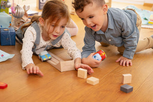 Two children playing on a wooden floor with HABA Cars and blocks.