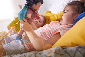 Two children lying on a bed, one holding a HABA William soft doll.