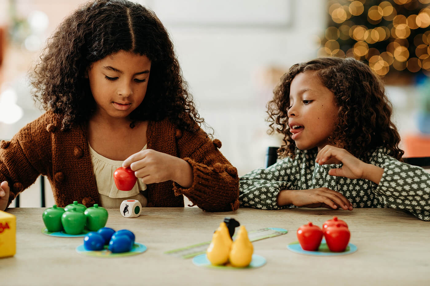 Two girls in front of a Christmas tree playing the HABA game First Orchard