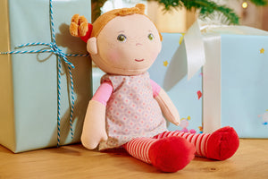 A plush Roya from HABA doll sitting next to two wrapped gifts under a Christmas tree.