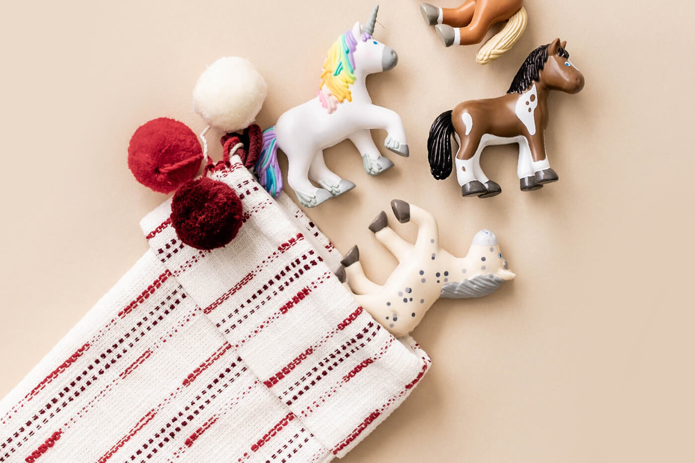 HABA Little Friends toy horses and unicorns on a beige surface with a woven stocking in the corner.