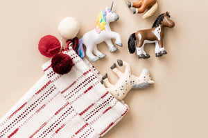 HABA Little Friends toy horses and unicorns on a beige surface with a woven stocking in the corner.